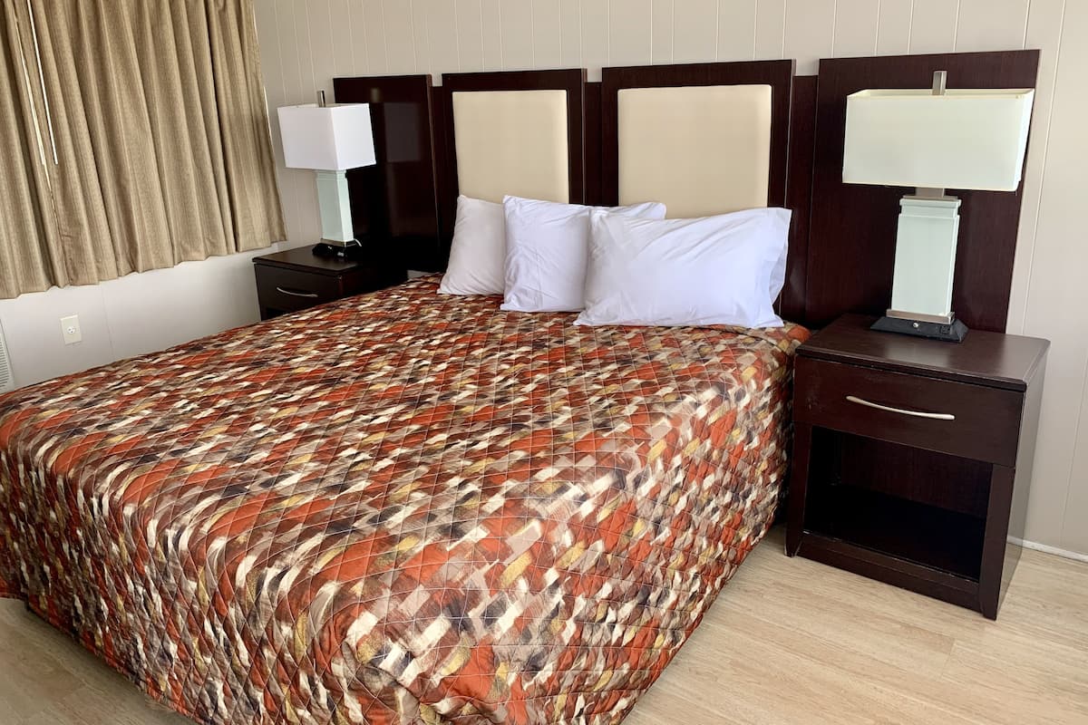 A hotel room with a large bed, two bedside tables with lamps, a headboard, and a curtain.