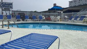 Uma área de piscina com cadeiras de descanso azuis e um letreiro para o Cabana Motel.