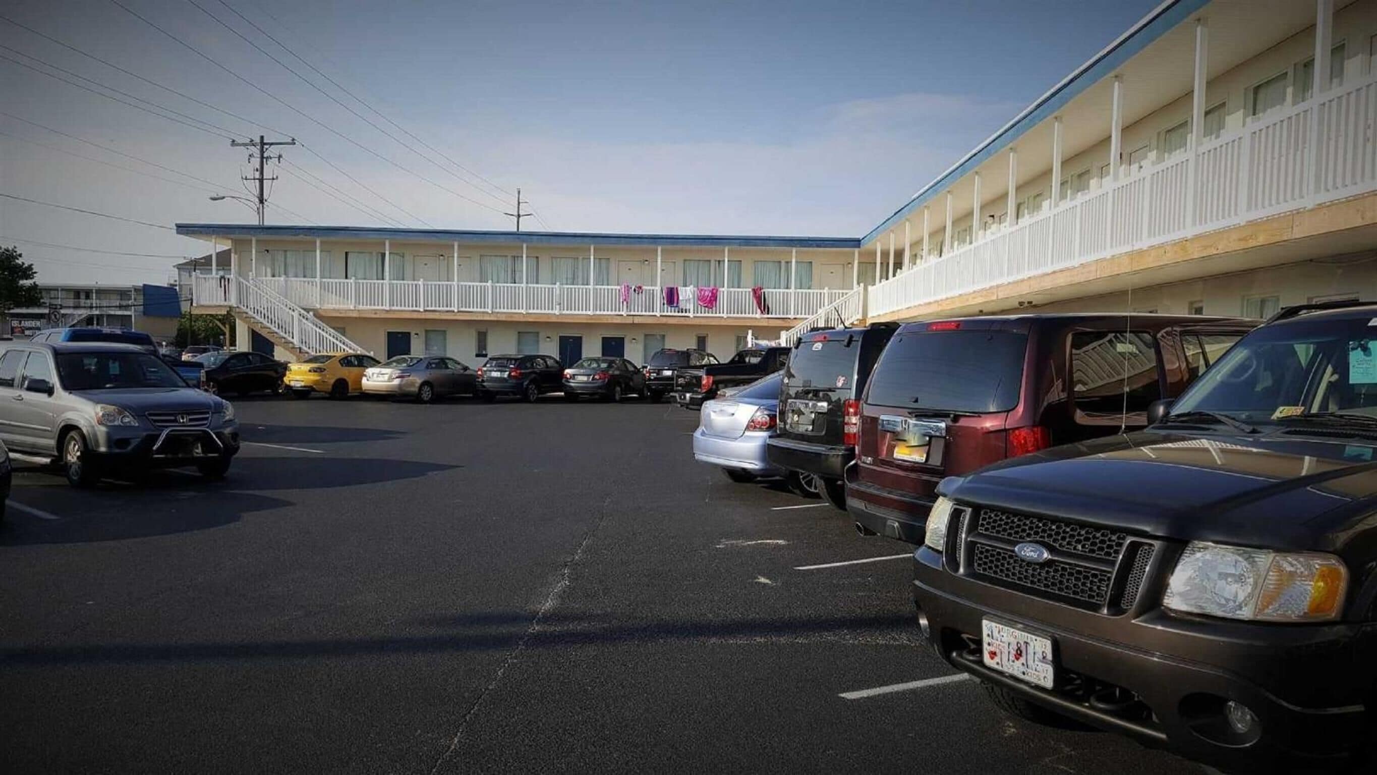 A parking lot with several cars and a building with a balcony in the background.
