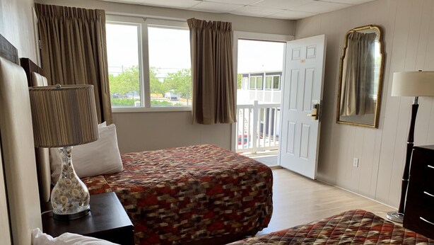 Quarto de hotel com duas camas, uma janela grande, uma porta, um espelho e um abajur.