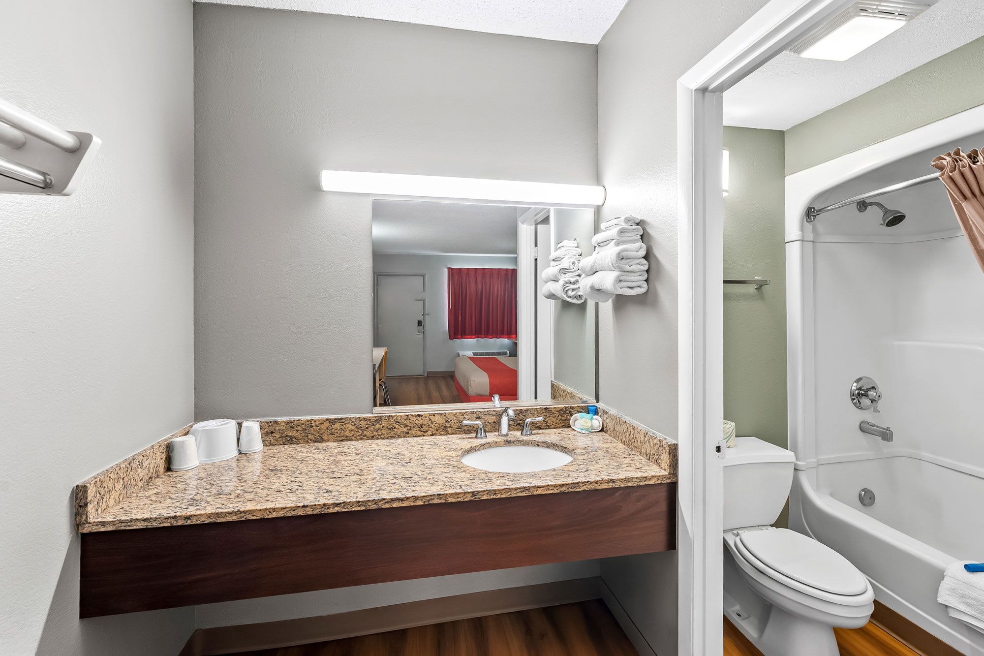 A modern bathroom with a granite countertop sink, a mirror, a toilet, and a shower.
