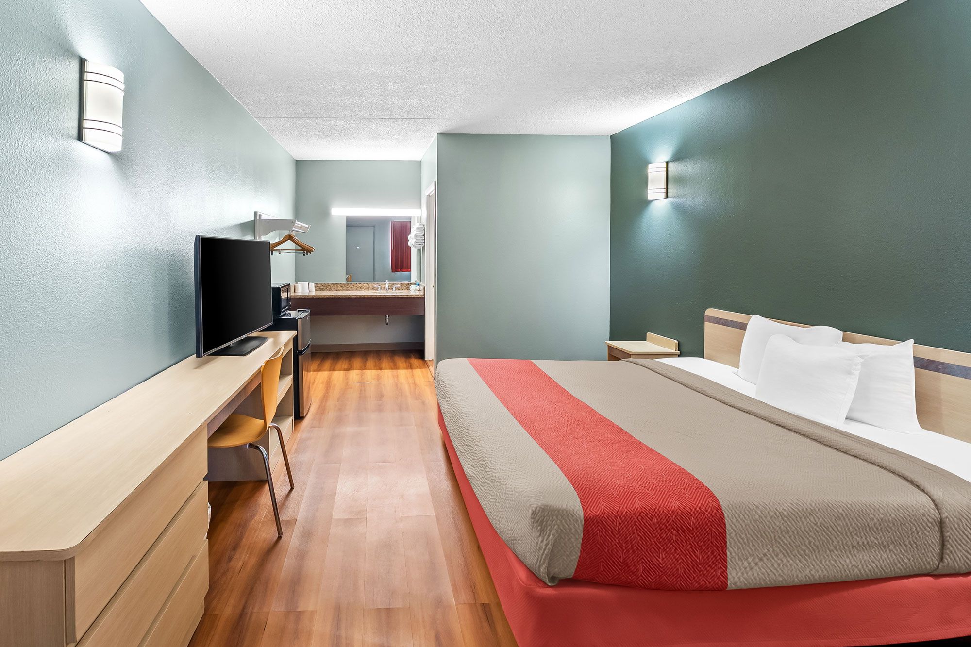 A hotel room with a bed, a desk, a television, and a bathroom visible in the background.