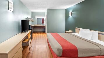 A hotel room with a bed, a desk, a television, and a bathroom visible in the background.