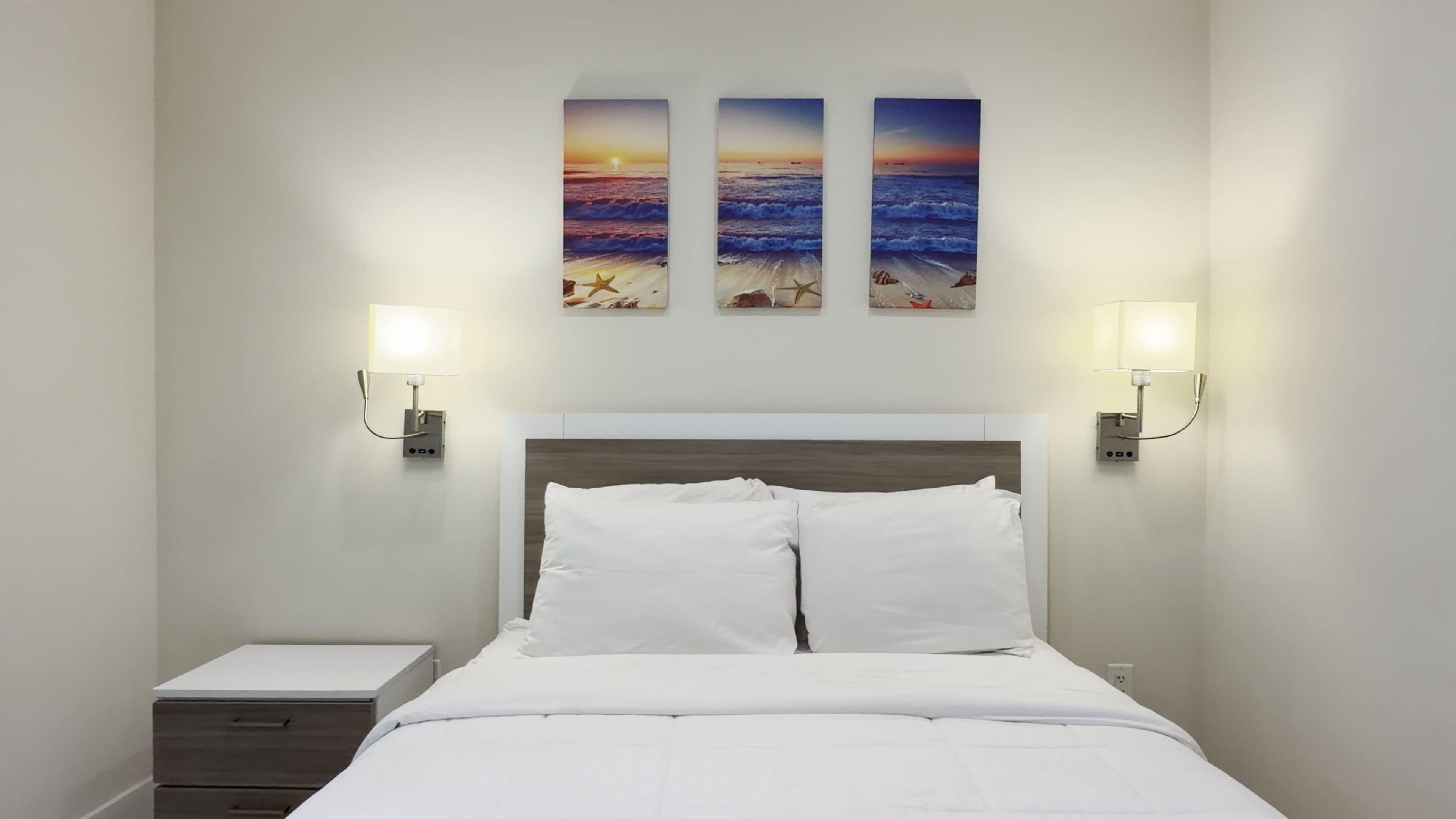 A hotel room with a bed, bedside tables, and wall-mounted artwork.