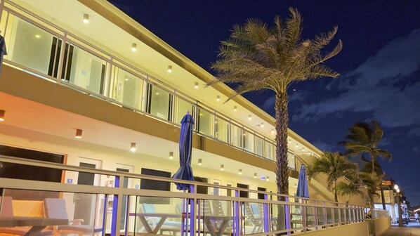 Un hotel con balcón, palmeras y mobiliario de exterior.