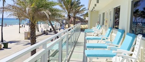 A balcony with sun loungers, a beach view, and palm trees.