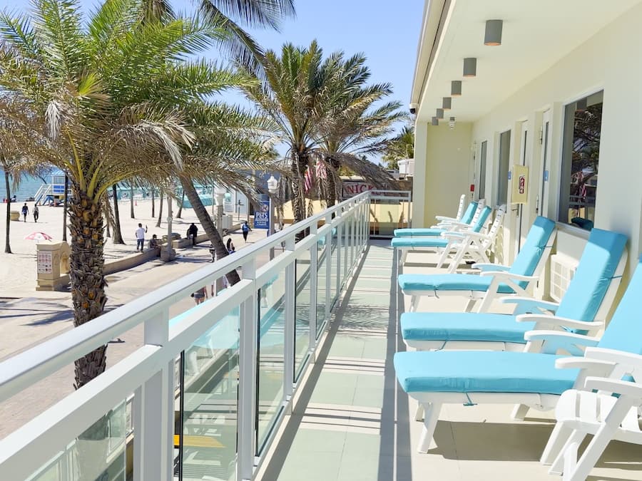 A balcony with sun loungers, a beach view, and palm trees.
