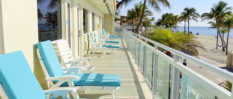 A balcony with sun loungers facing a beach, palm trees, and a clear view of the ocean.