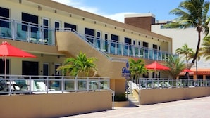 Un hotel de diseño moderno, con una escalera central, asientos exteriores con sombrillas rojas y palmeras.