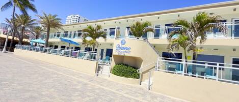 A hotel named 'Diane Oceanfront Suites' with a clear blue sky, palm trees, and a paved walkway.