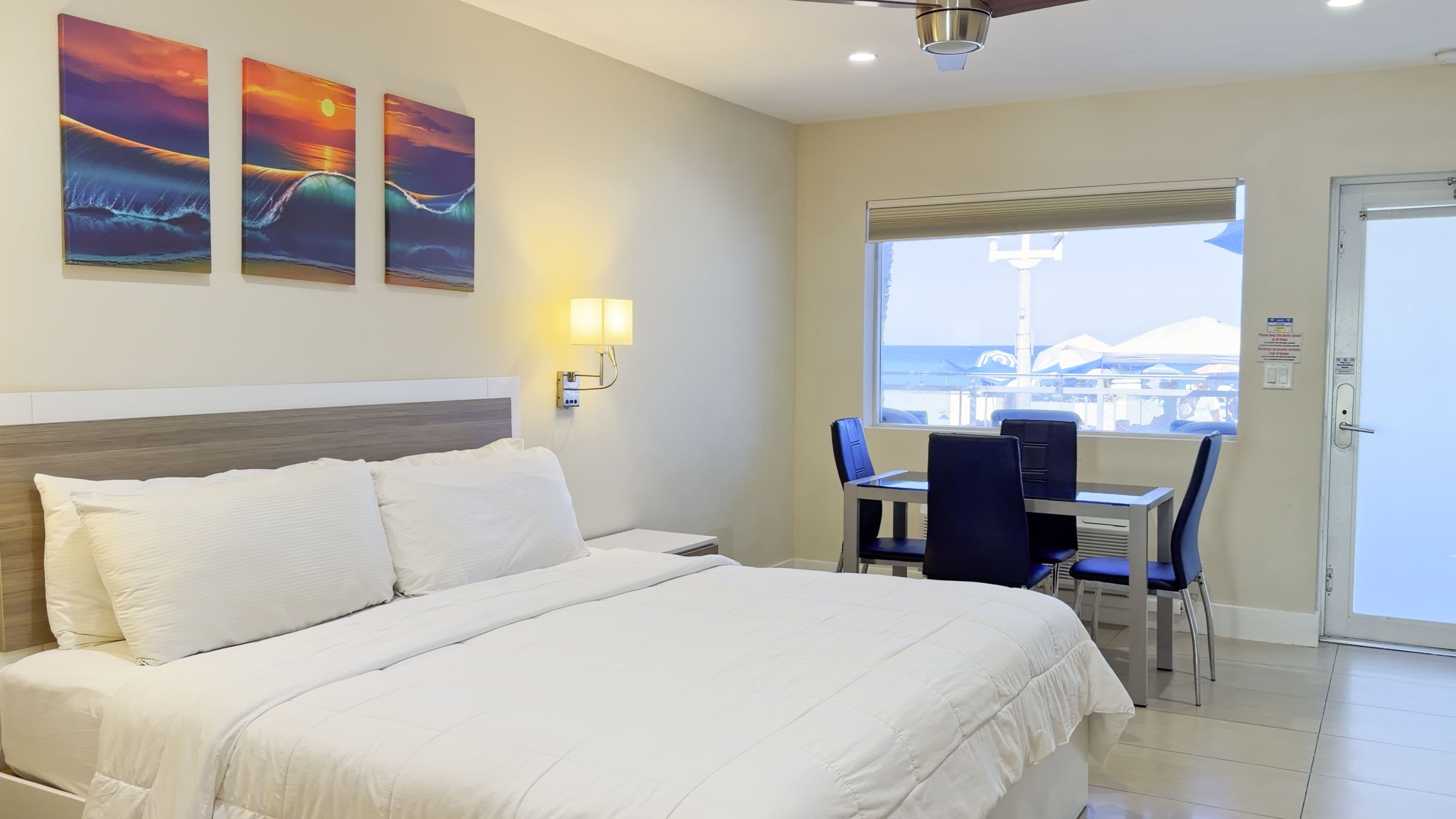 A hotel room with a bed, a desk with chairs, a window with a view, and wall-mounted artwork.