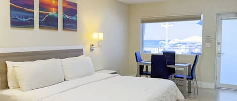 A hotel room with a bed, a desk with chairs, a window with a view, and wall-mounted artwork.