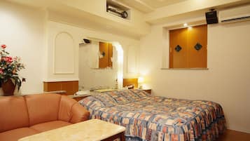 A hotel room with a bed, a small table, a sofa, and a potted plant.