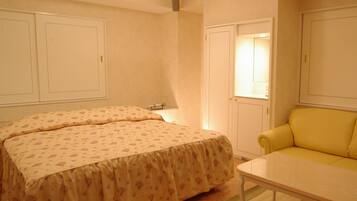 A bedroom with a bed, a yellow armchair, a small table, and a closet.