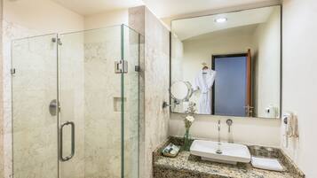 Un baño moderno con ducha envuelta en vidrio, pared con mosaico de mármol, encimera de granito, lavamanos y un espejo grande.