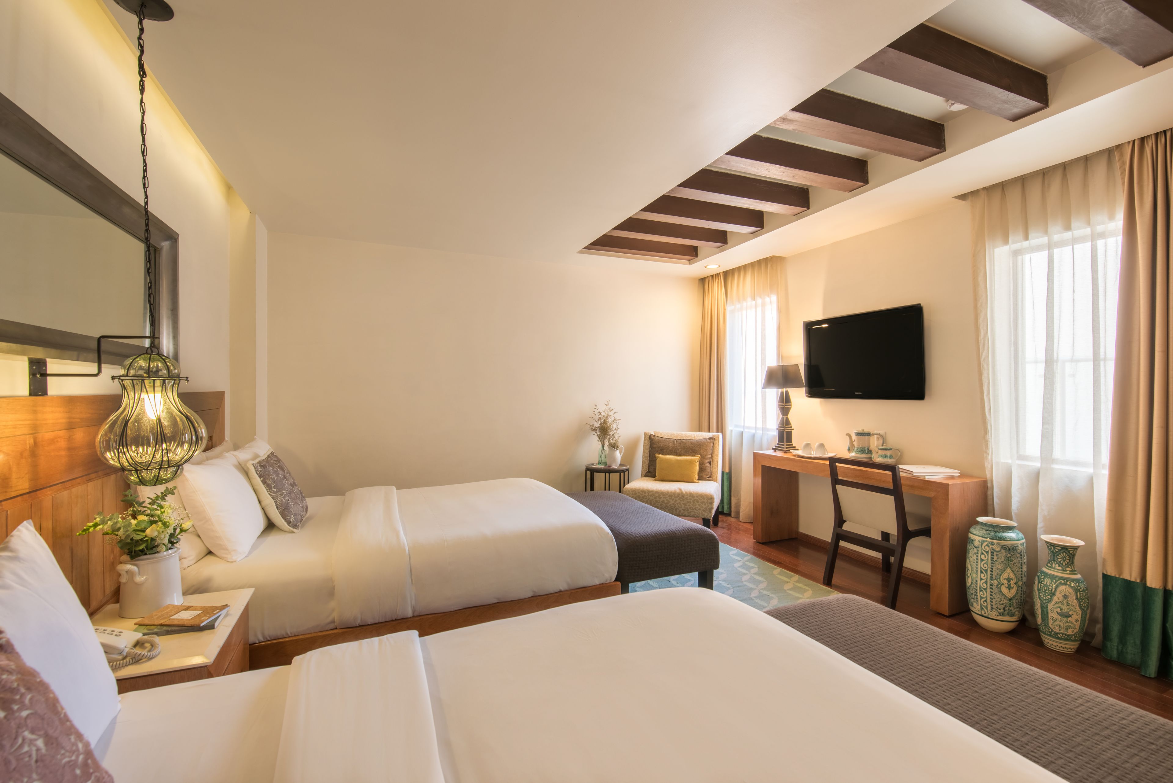 Une chambre d’hôtel avec deux lits, un bureau, une télévision et une fenêtre avec des rideaux.