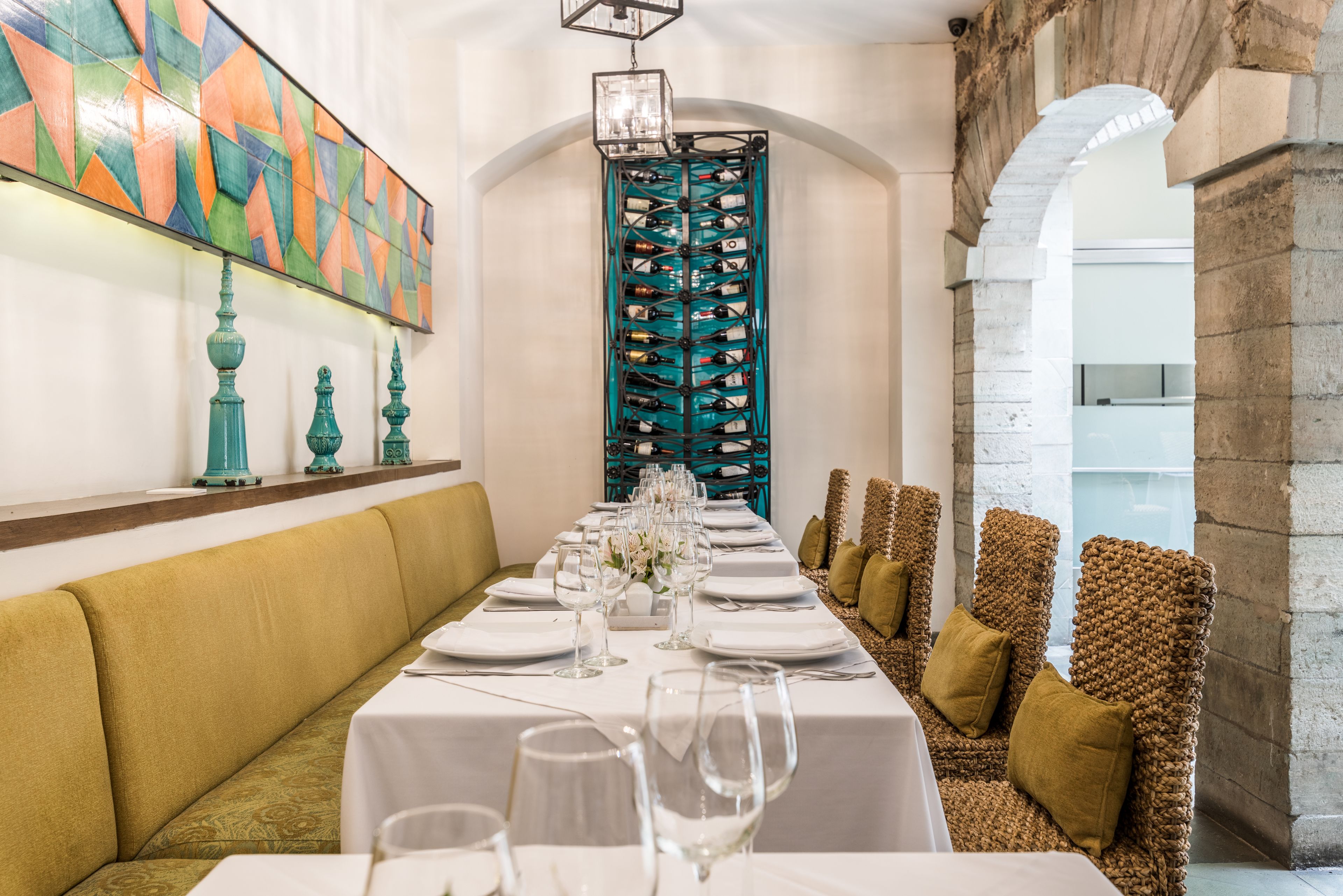 Una larga mesa de comedor lista para una comida, con una estantería decorativa para vino al fondo.
