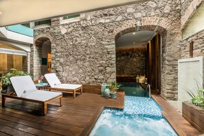 A stone-walled outdoor area with a wooden deck, two lounge chairs, a small pool, and potted plants. - Edelmira Hotel Boutique (Guanajuato)