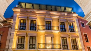 Un edificio de varios pisos con una entrada imponente, ventanas amplias y un balcón con barandilla de hierro forjado.