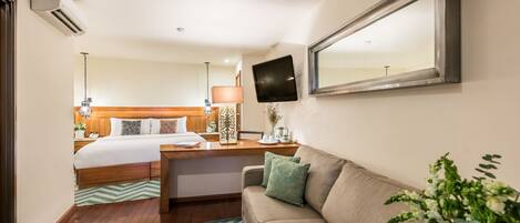 Habitación de hotel con cama, sofá, televisión y espejo.