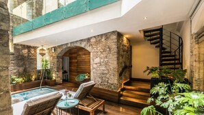 Un área de piscina interior moderna con un arco de piedra, suelo de madera, sillones de descanso y una escalera de caracol.