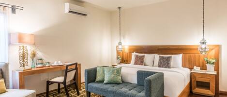Une chambre d’hôtel avec un lit, un bureau, une chaise, un canapé et un tapis à motifs.