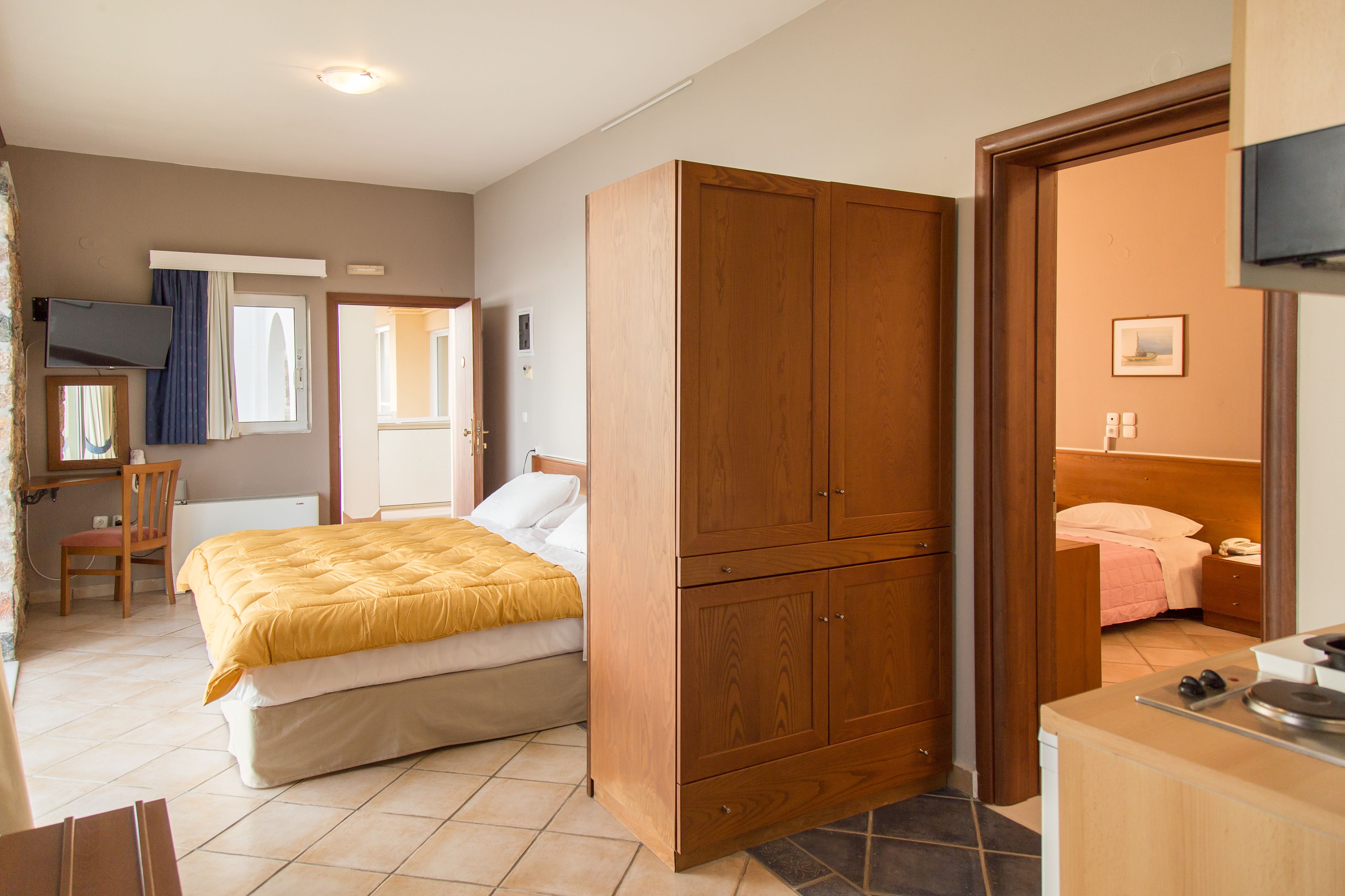 A bedroom with a bed, wooden wardrobe, a desk with a chair, and a television.