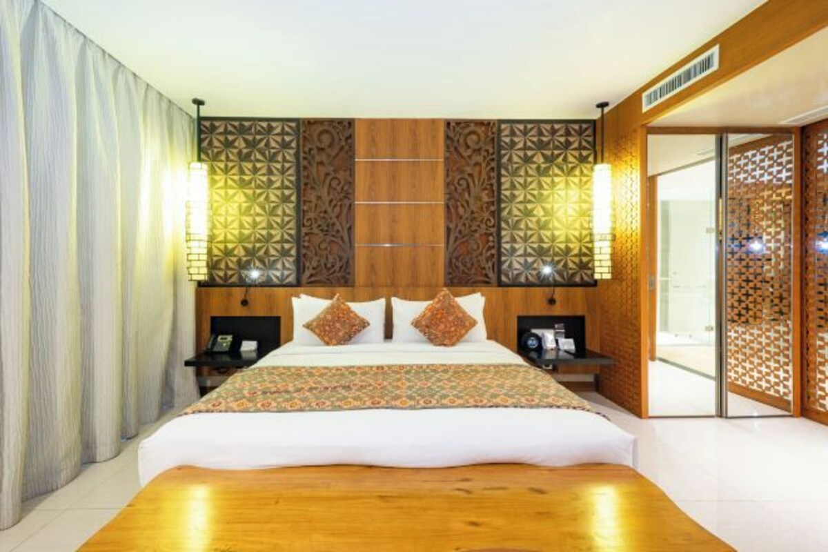 A hotel room with a large bed, wooden headboard, decorative wall panels, and a sliding door.
