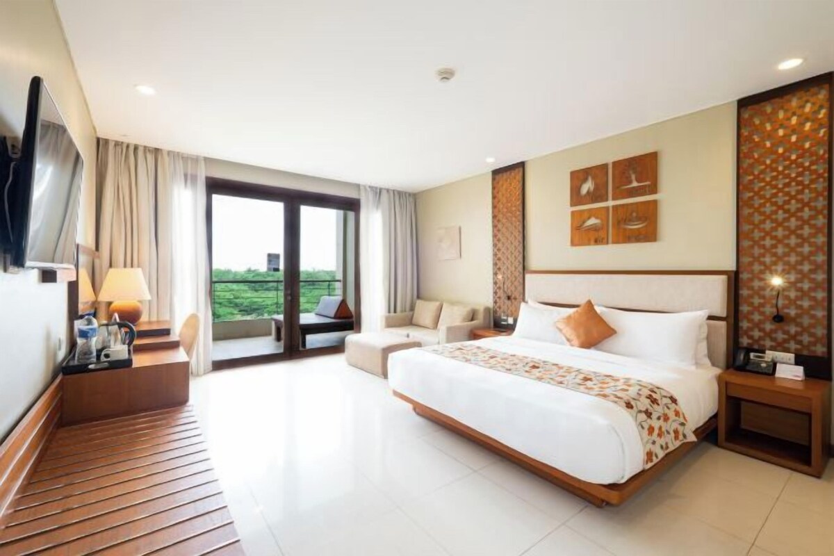 A hotel room with a large bed, a sofa, a TV, and a balcony with a view.
