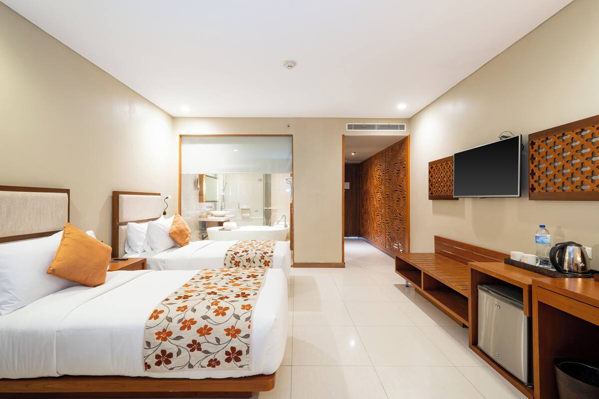 A hotel room with two beds, a TV, a coffee maker, and a small kitchenette.