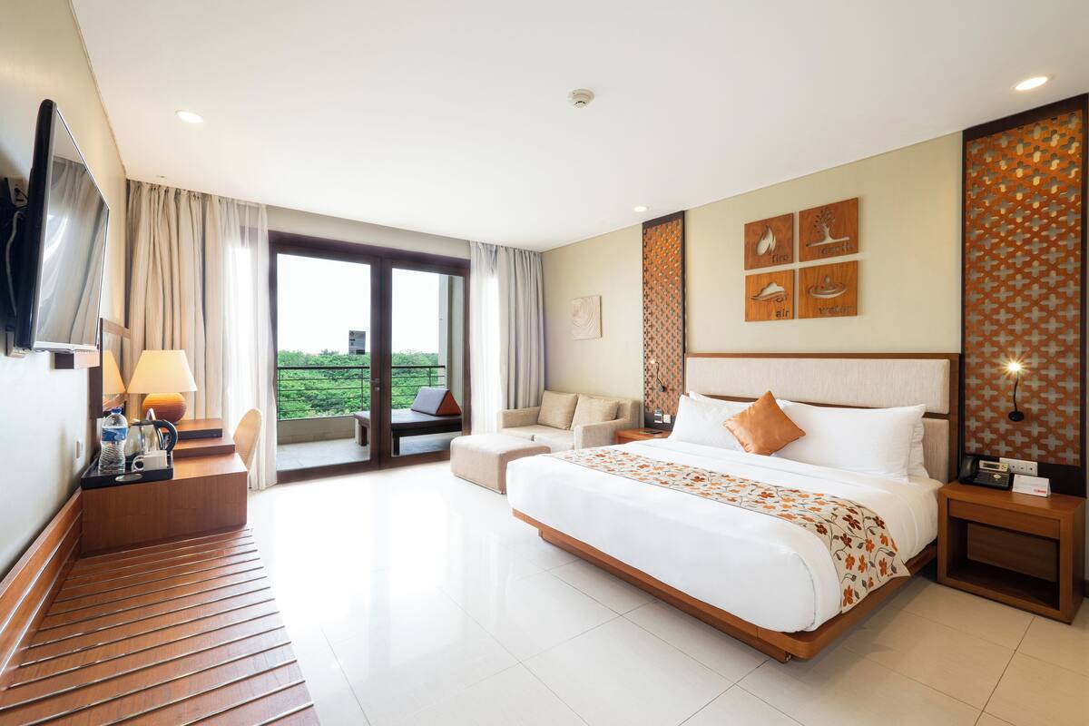 A modern hotel room with a large bed, a sofa, a desk with a lamp, and a TV.