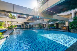 A swimming pool with a tiled deck, surrounded by lounge chairs and potted plants.