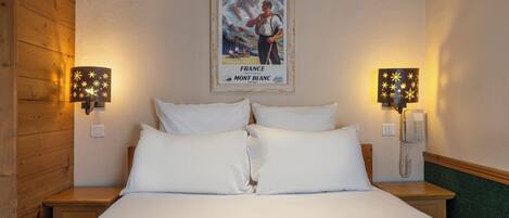Una habitación de hotel con una cama, dos lámparas de noche, un cuadro en la pared y un teléfono en la mesita.