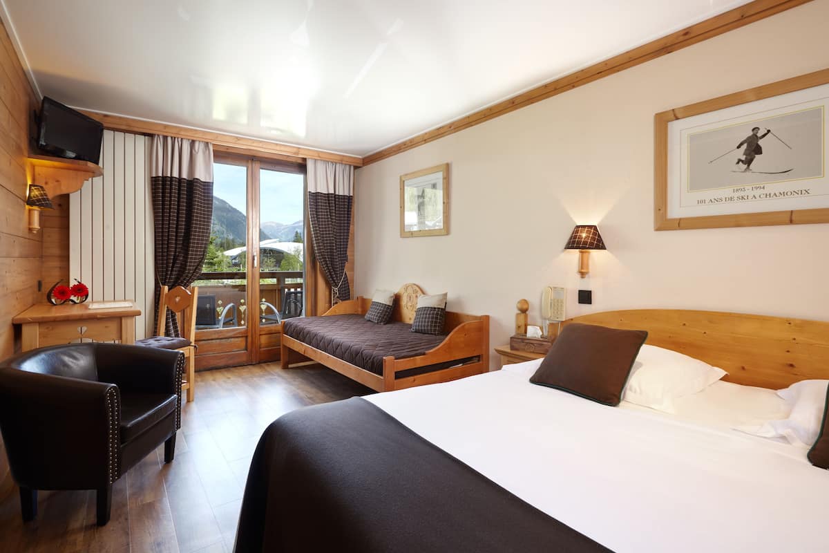 Een hotelkamer met een houten bed, een leren fauteuil, een bureau met een lamp en een raam met gordijnen.