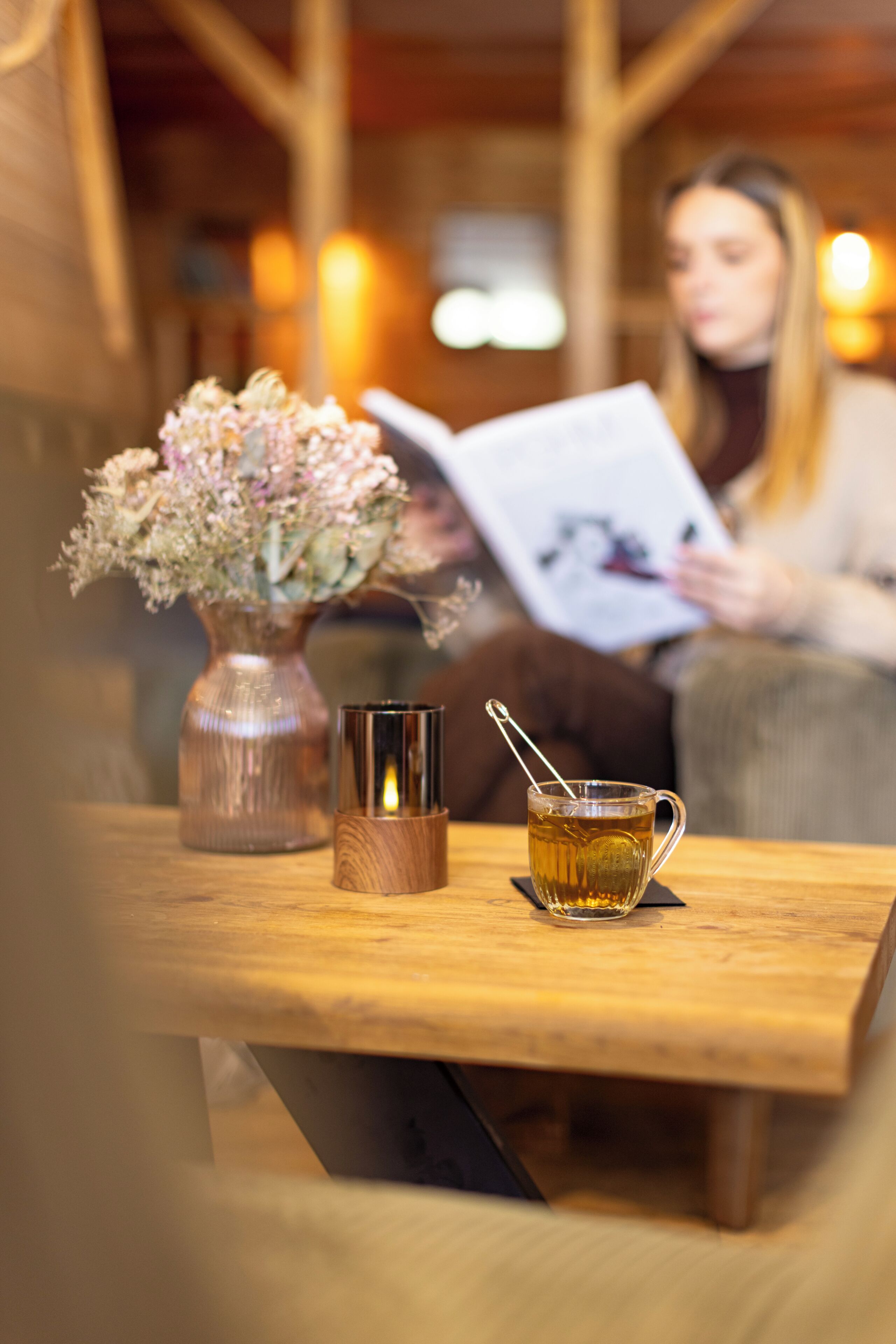 Una mesa de madera con un jarrón de flores, una vela y una taza de té.