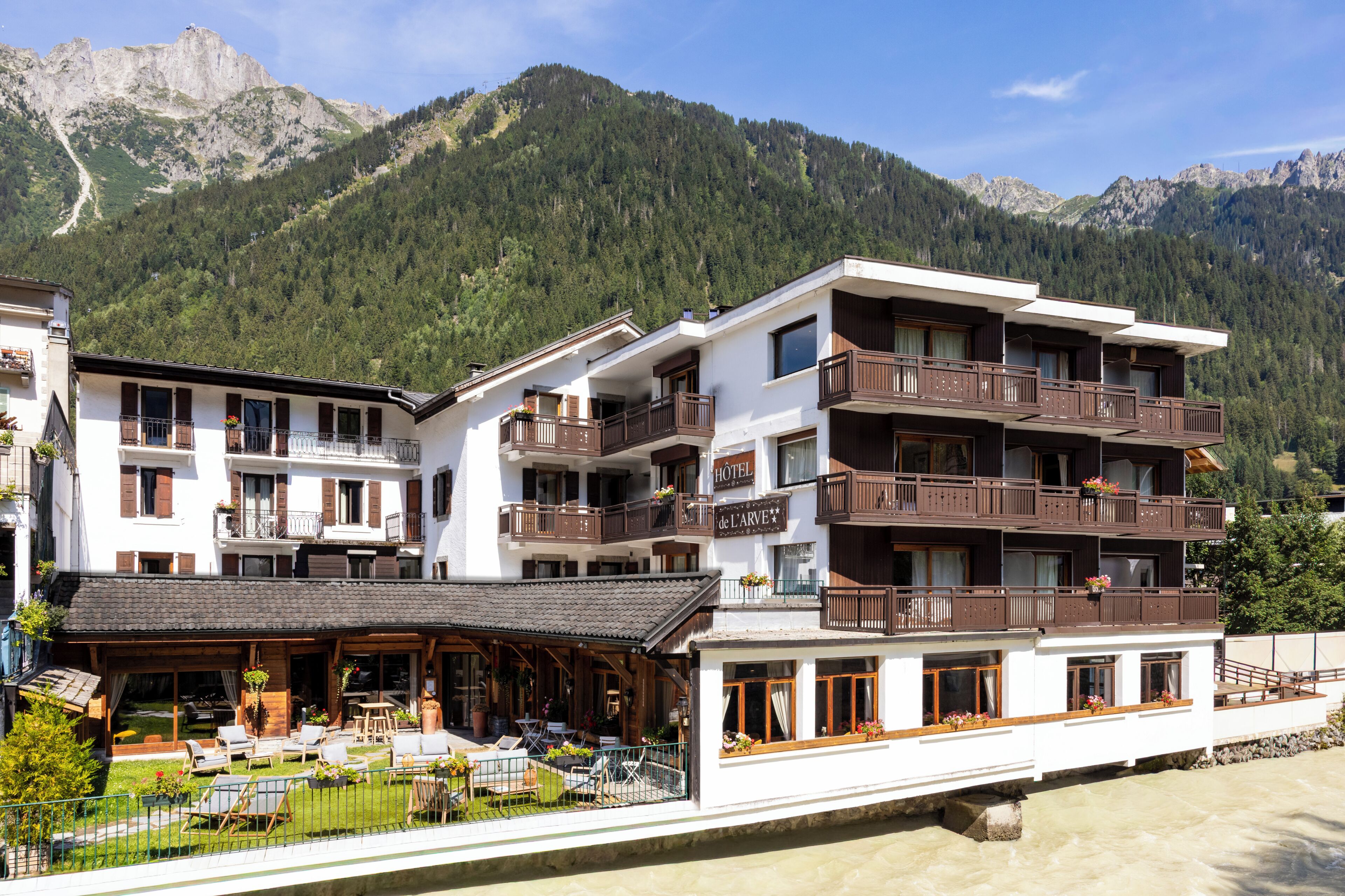 Een hotel met meerdere balkons, een terras met buitenmeubilair en een bergachtig landschap op de achtergrond.