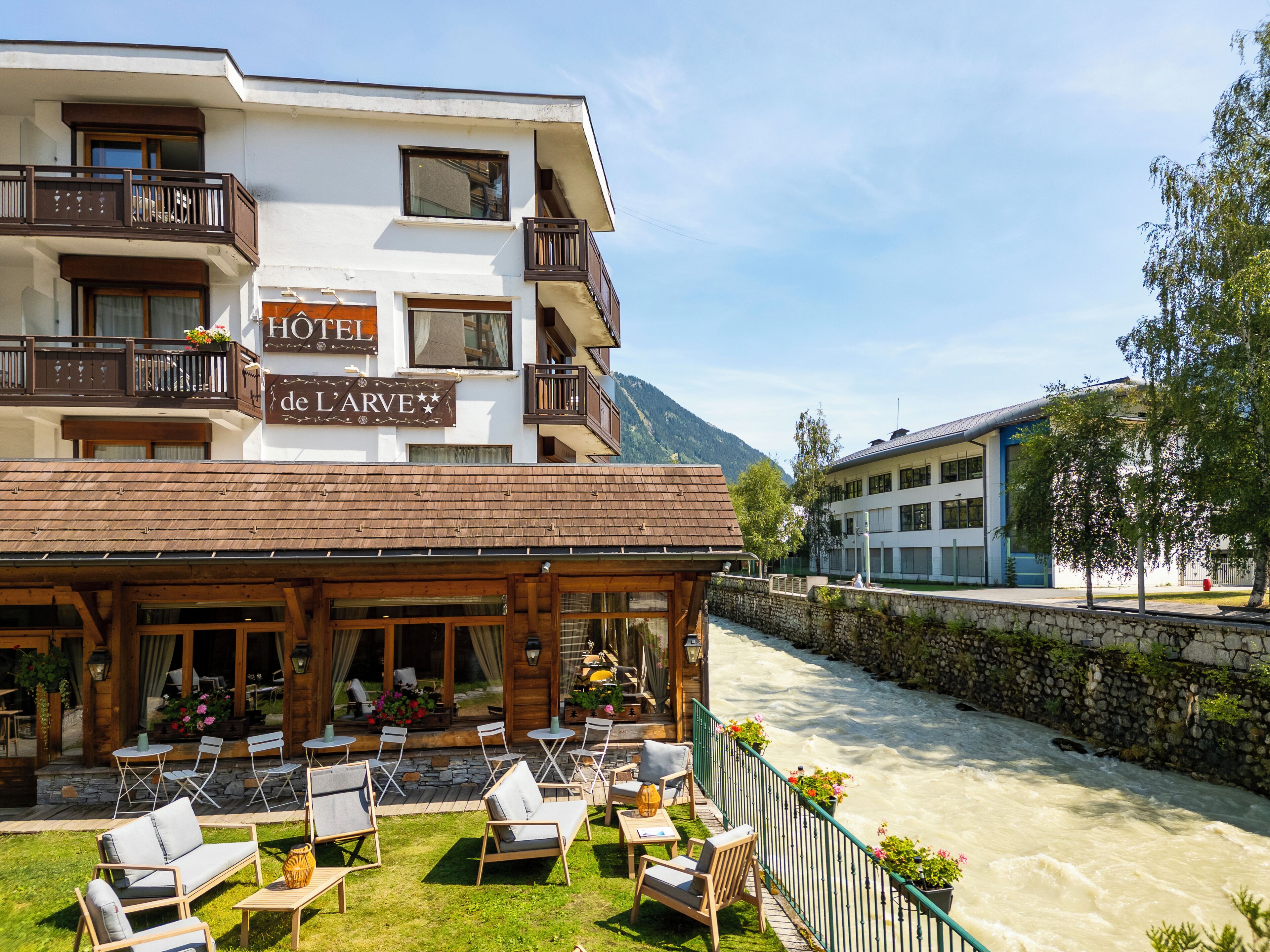 A hotel with a balcony, outdoor seating, and a view of a river.