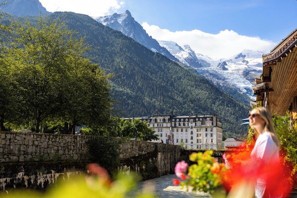 A historic building with a stone facade, a river in the foreground, and snow-capped mountains in the background. - Hôtel de l'Arve by HappyCulture (Chamonix-Mont-Blanc)