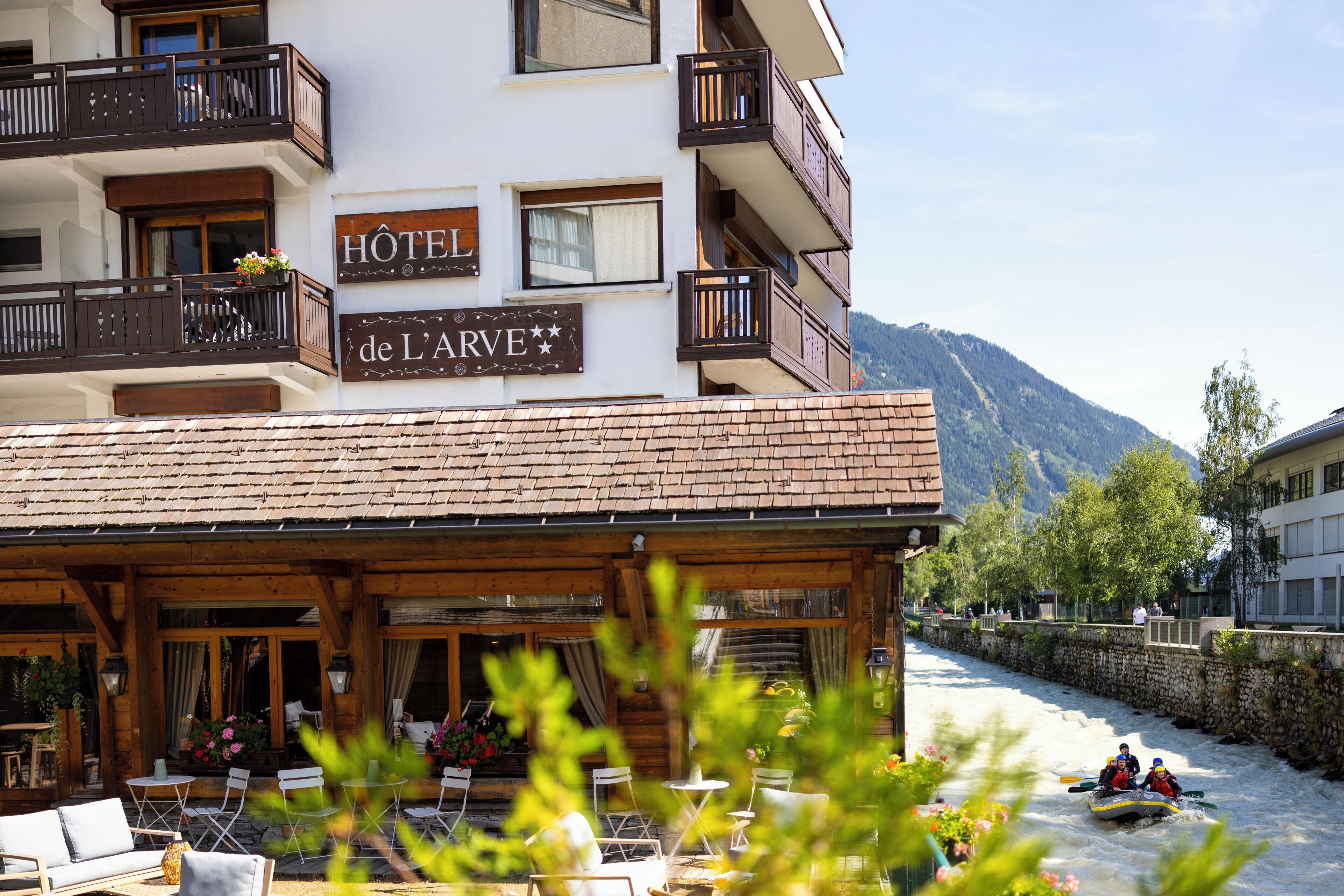 Ein Hotel mit einem Schild, auf dem 'HOTEL de L'ARVE' steht, und einer Flusslandschaft, in der Menschen mit Raft unterwegs sind.