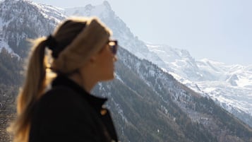A person holding a glass with a beverage, overlooking a mountainous landscape with a building in the background.