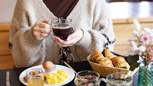Una persona sentada a una mesa con diversos alimentos para el desayuno, como huevos, pan y fruta.