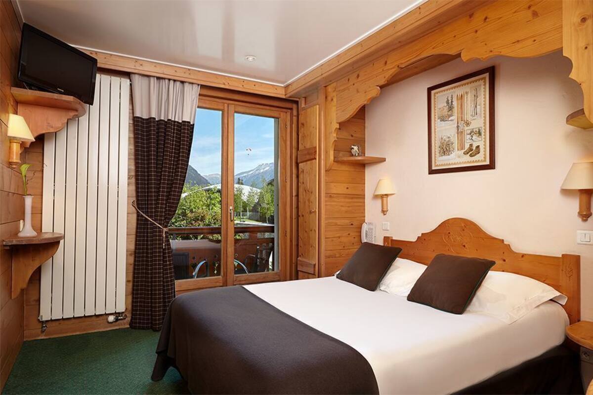 Een houten kamer met een bed, een televisie en een raam met gordijnen.