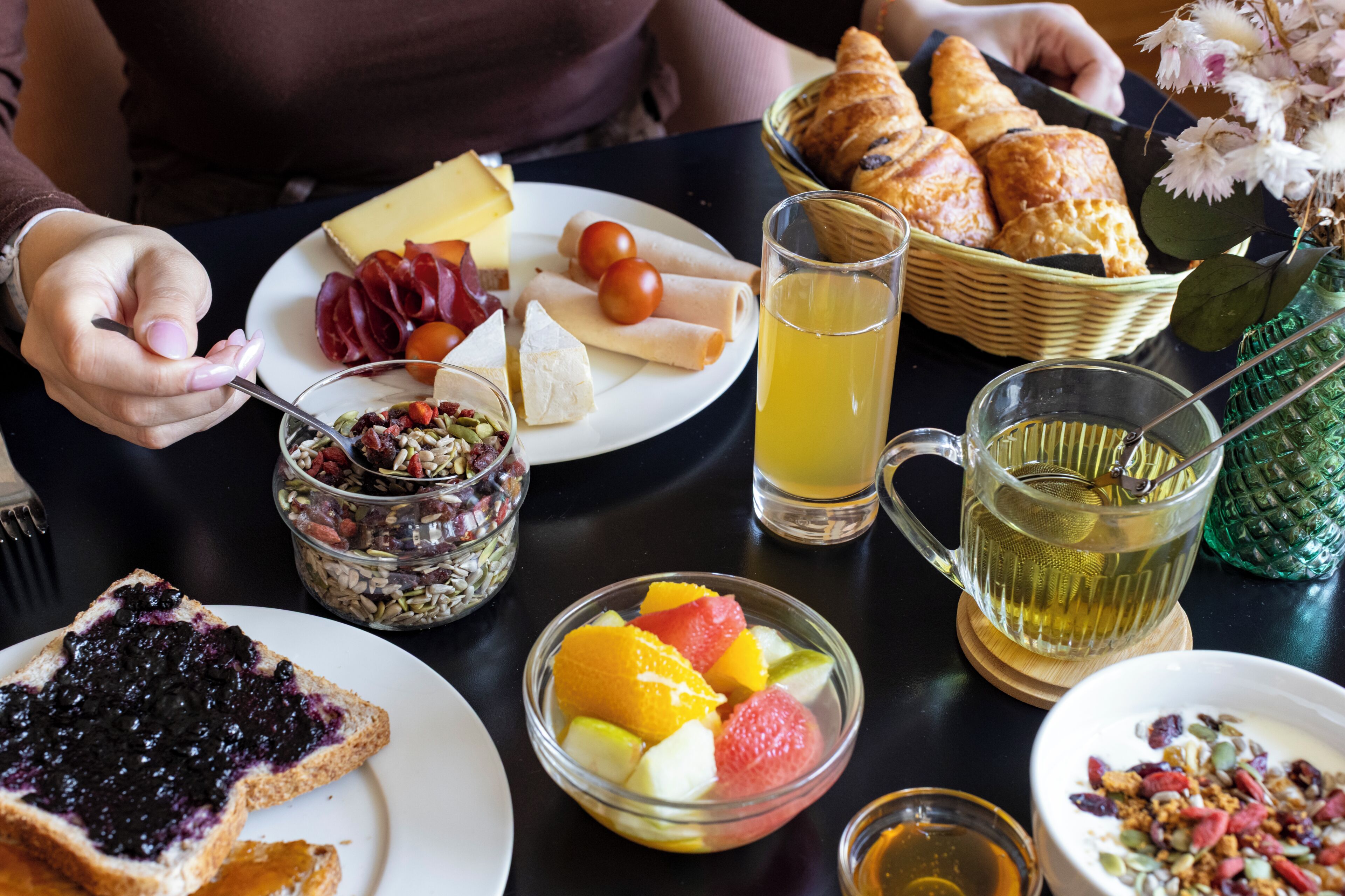 A breakfast table with various food items, a glass of juice, and a teapot.