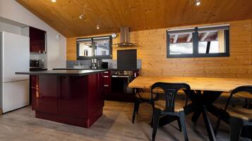 A modern kitchen with wooden ceiling, a central island, and a dining area with black chairs.