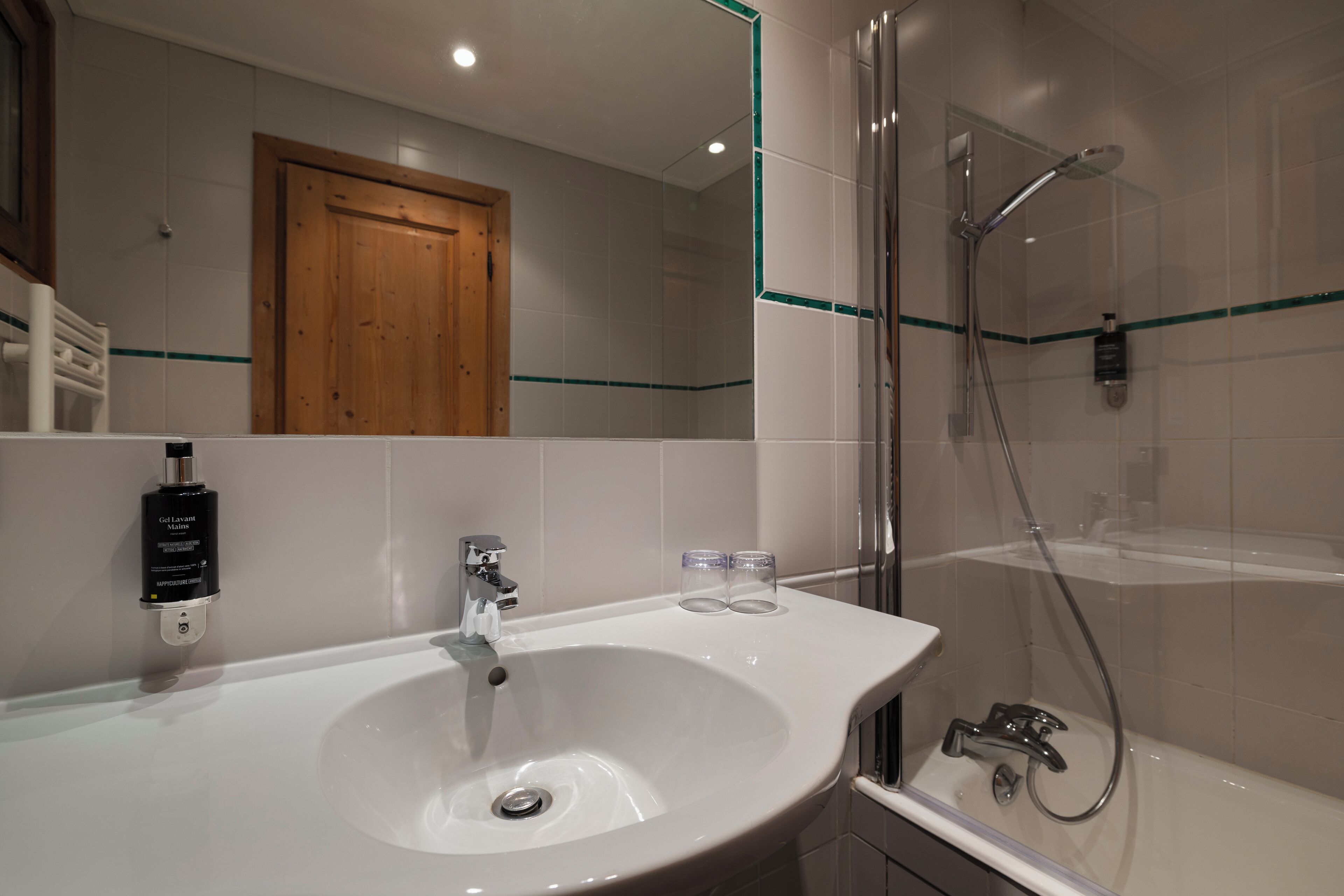 Een badkamer met een witte wastafel, een spiegel, een douche en een houten deur.