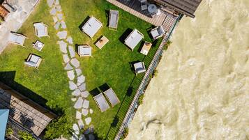 An aerial view of a riverside property with a patio area featuring outdoor seating and a stone pathway.