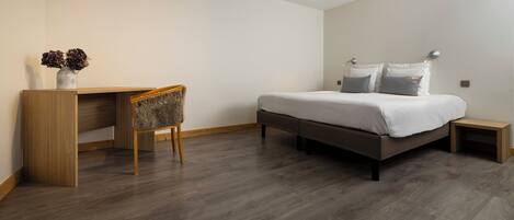 A bedroom with a bed, bedside table, chair, and a desk with a vase of flowers.