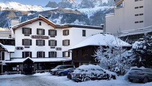 Un hotel con un letrero que dice "Hotel de l'Arc" en un paisaje nevado con montañas al fondo.