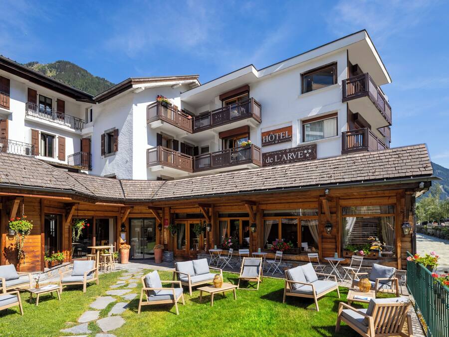 Un hotel con un área de estar exterior cubierta, varios balcones y vistas a las montañas.