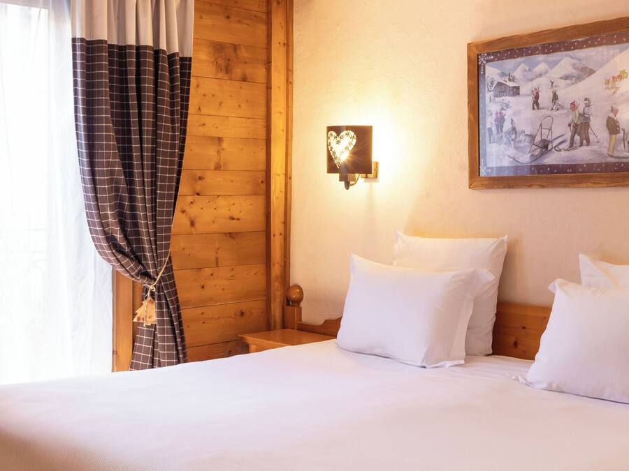 Una habitación de madera con una cama, almohadas blancas, una lámpara de pared y un cuadro enmarcado.